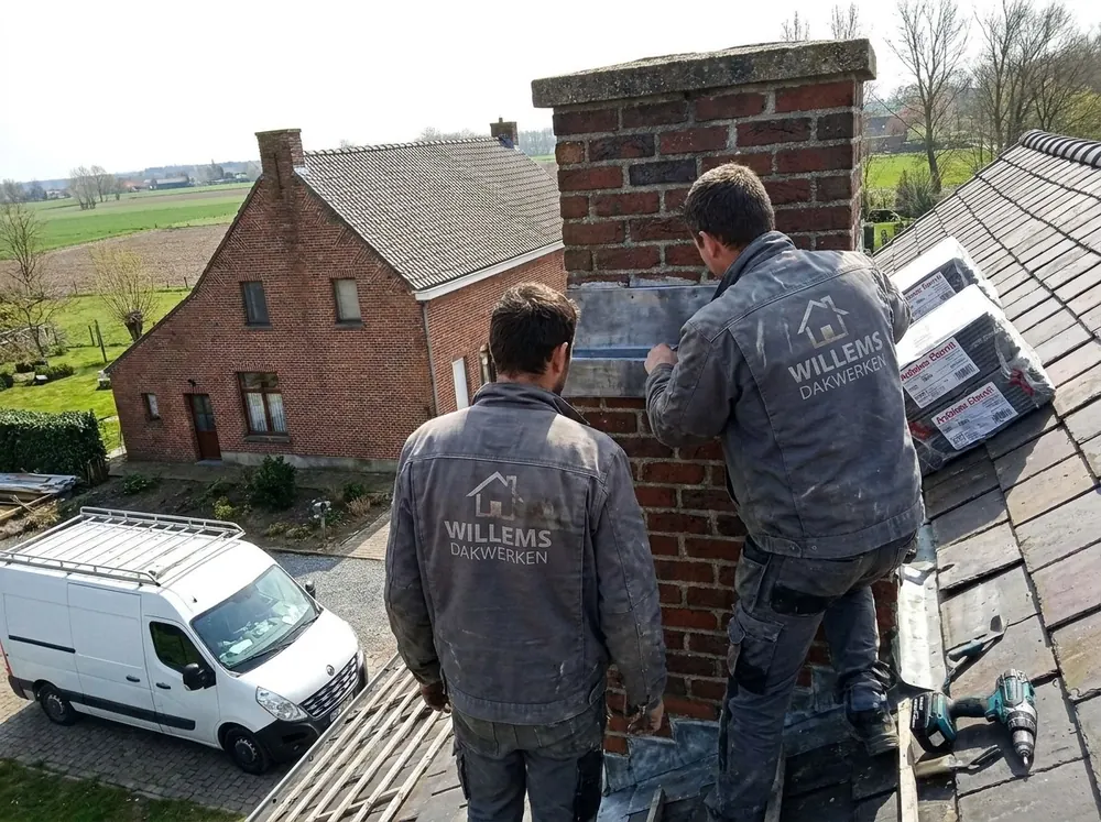 Dakwerkers van Willems Dakwerken herstellen een bakstenen schoorsteen op een leien dak